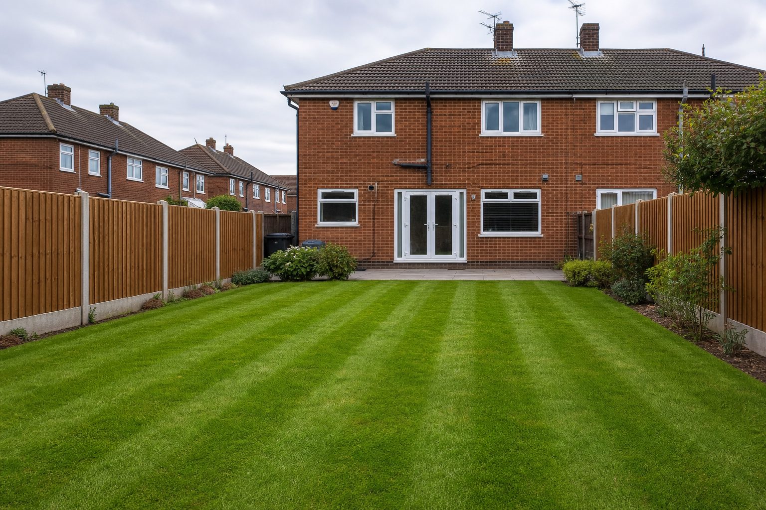 Freshly striped green back lawn behind a red-brick semi-detached house
